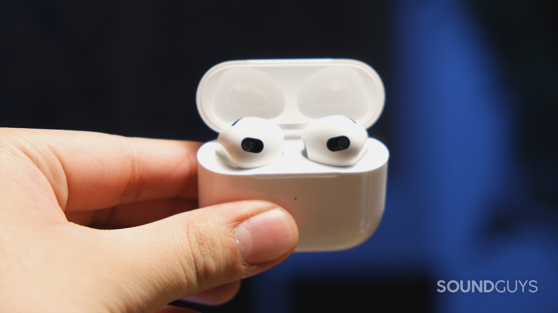 Apple AirPods 3rd Generation_6 A hand holds a Apple AirPods (3rd generation) case with the earbuds in place and embedded sensors in view.
