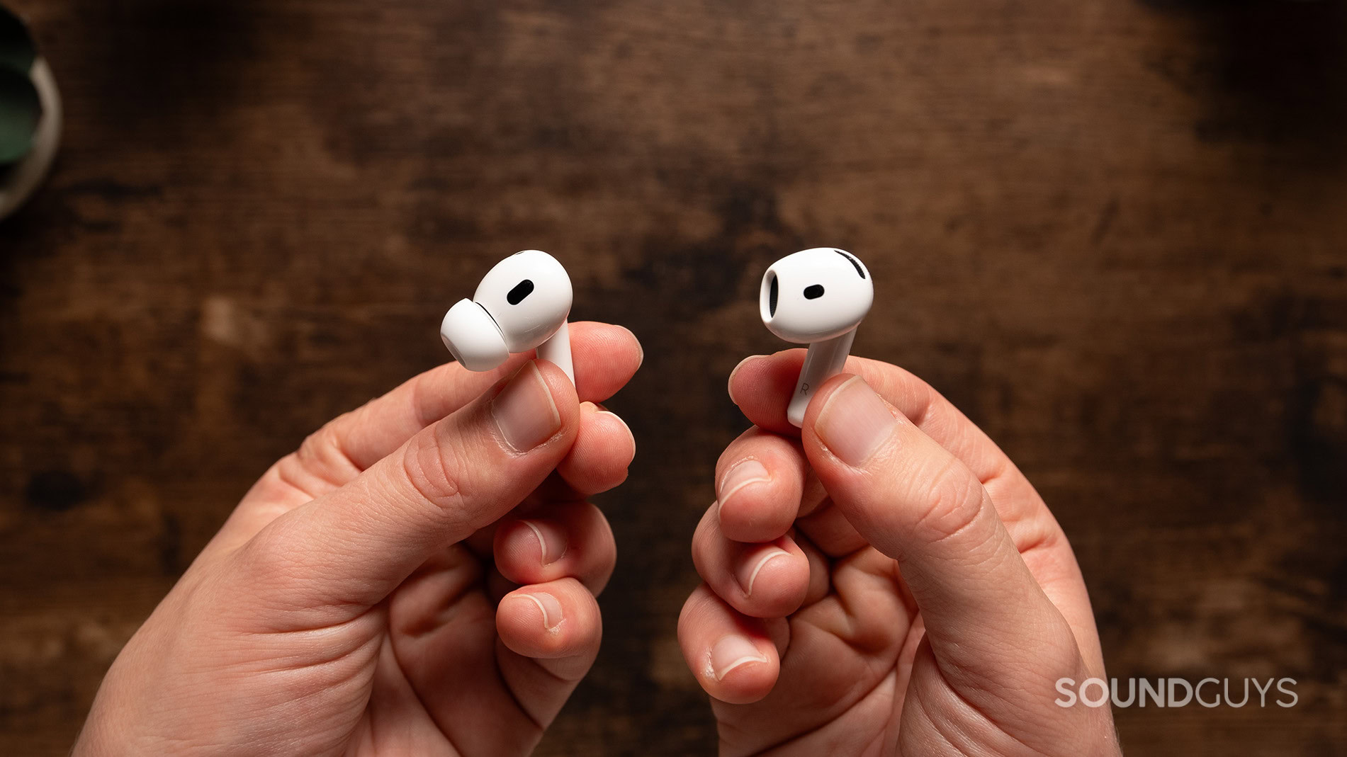 AirPods 4 vs AirPods Pro 2 earbuds in hand 3 One hand holds an AirPods 4 earbud while one hand holds an AirPods Pro 2 earbud.