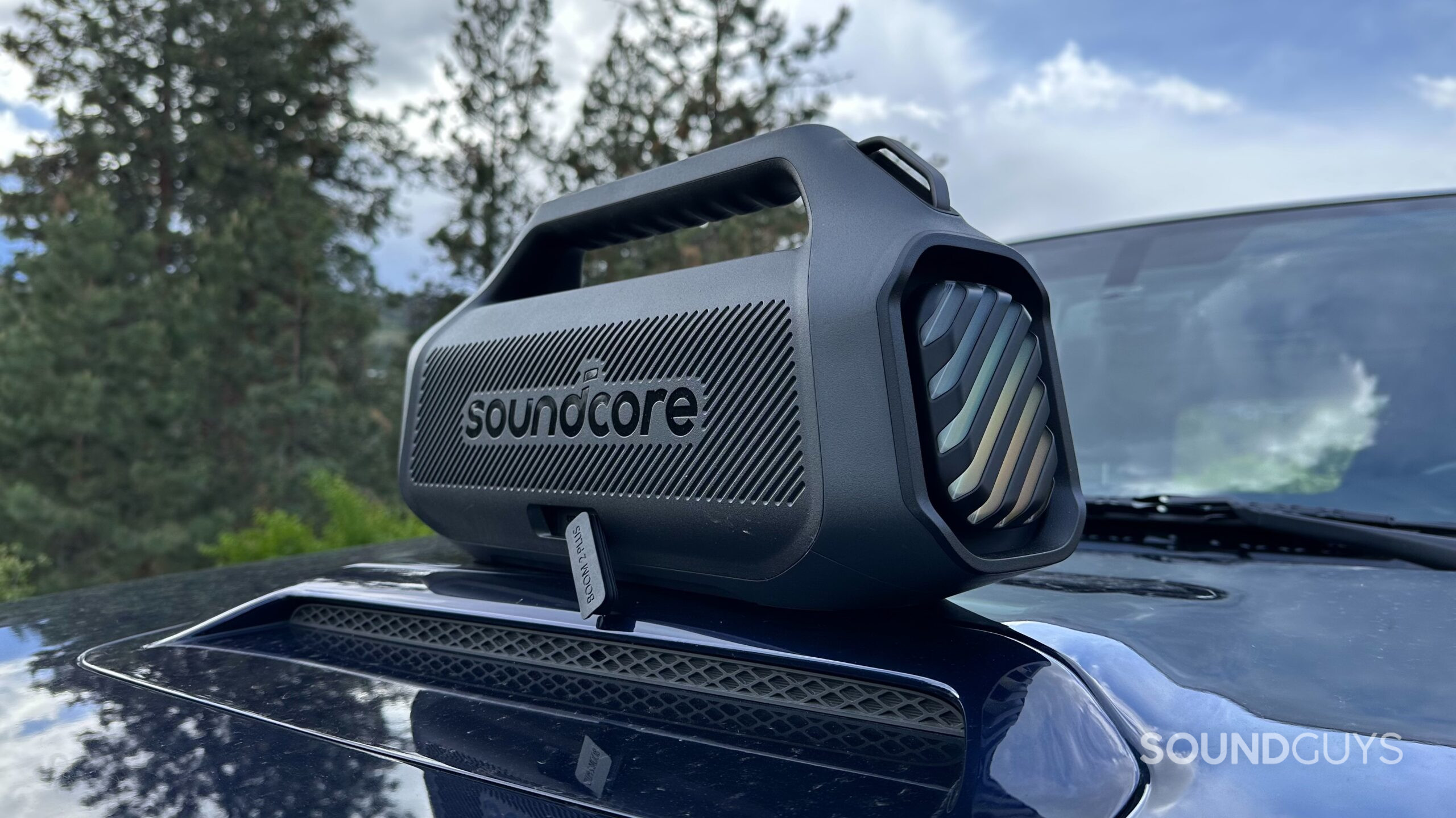 Anker Soundcore Boom 2 Plus 10 An Anker Soundcore Boom 2 Plus placed on top of an automobile hood, backside with open USB cover facing the camera.