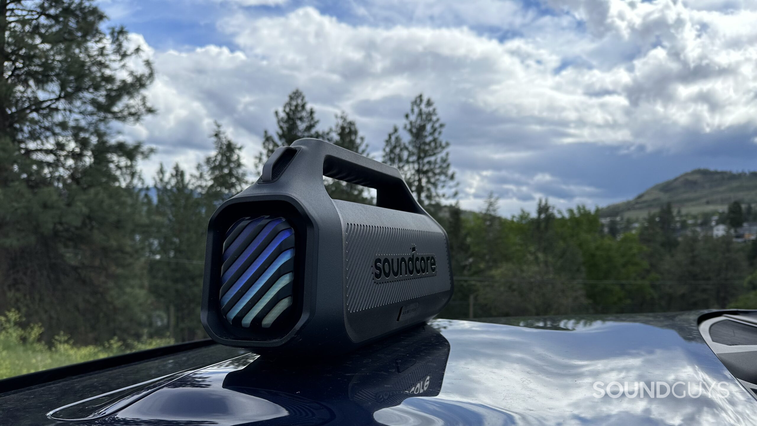 Anker Soundcore Boom 2 Plus 11 An Anker Soundcore Boom 2 Plus placed on top of an automobile hood, backside facing the camera.