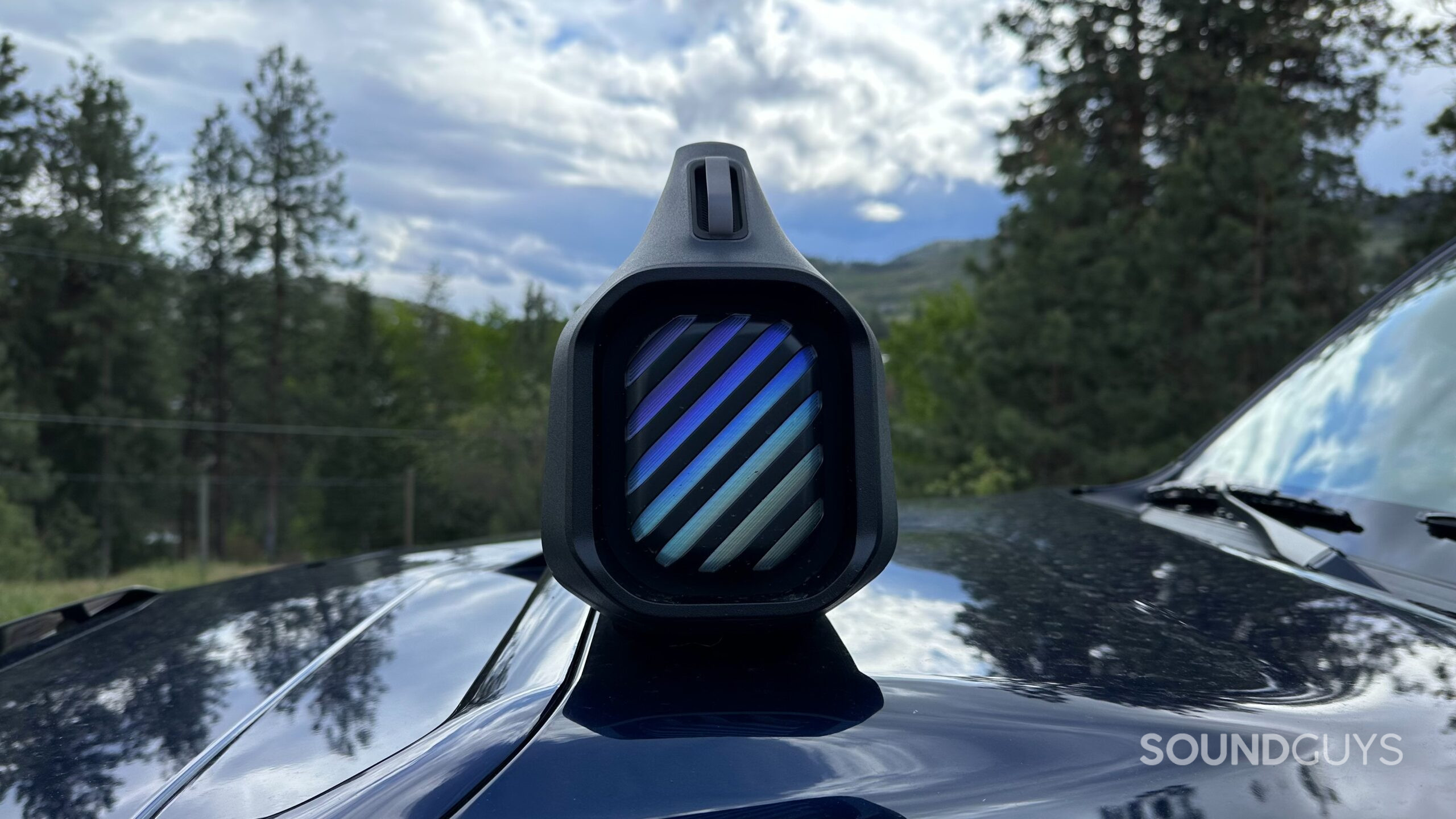 Anker Soundcore Boom 2 Plus 6 An Anker Soundcore Boom 2 Plus placed on top of an automobile hood, angled towards the camera, showing the lit-up passive radiator.