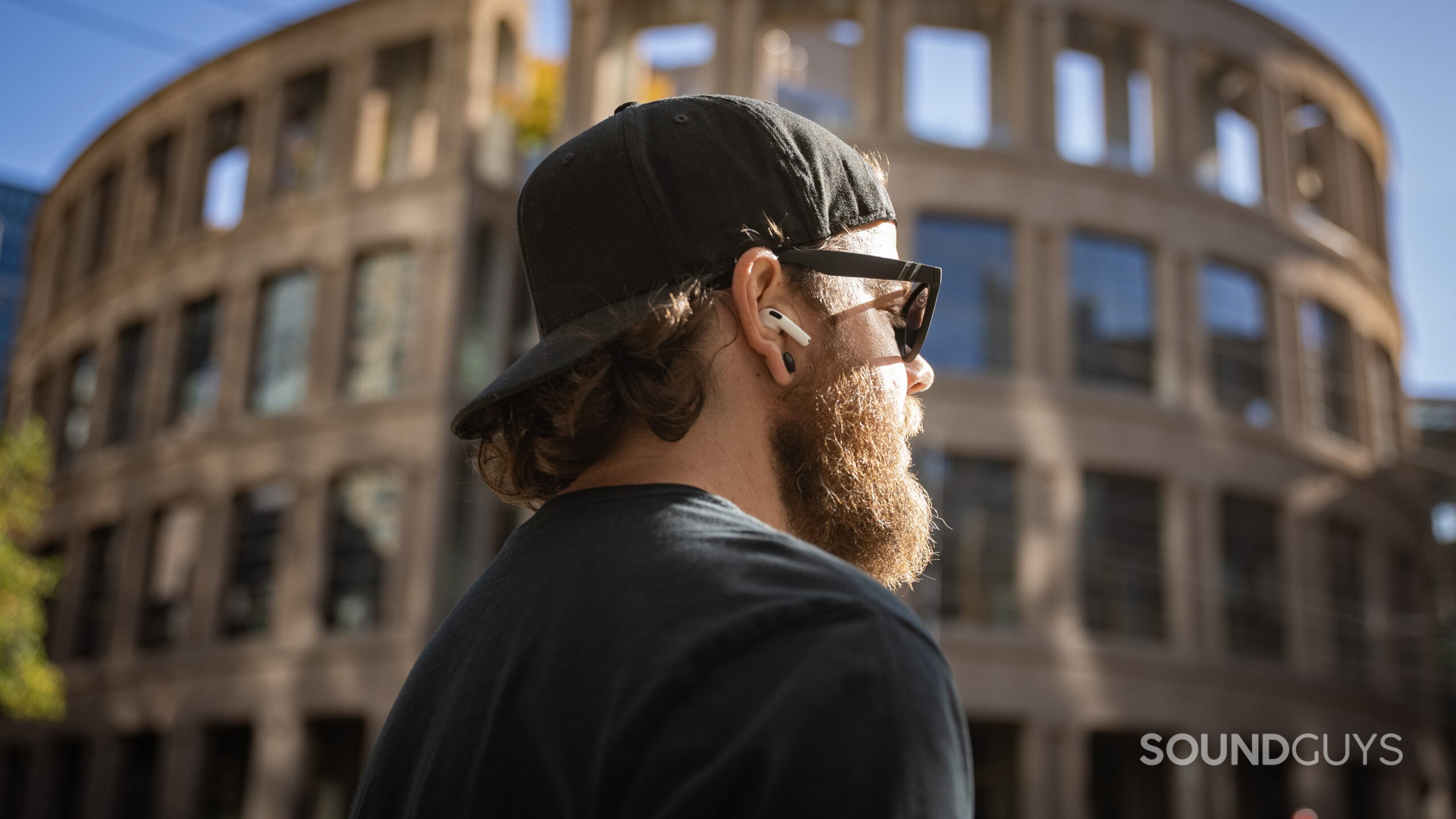 Apple AirPods 4 side profile man wearing outside library profile A man wears the AirPods 4 with Active Noise Cancellation outdoors in front of a large building.