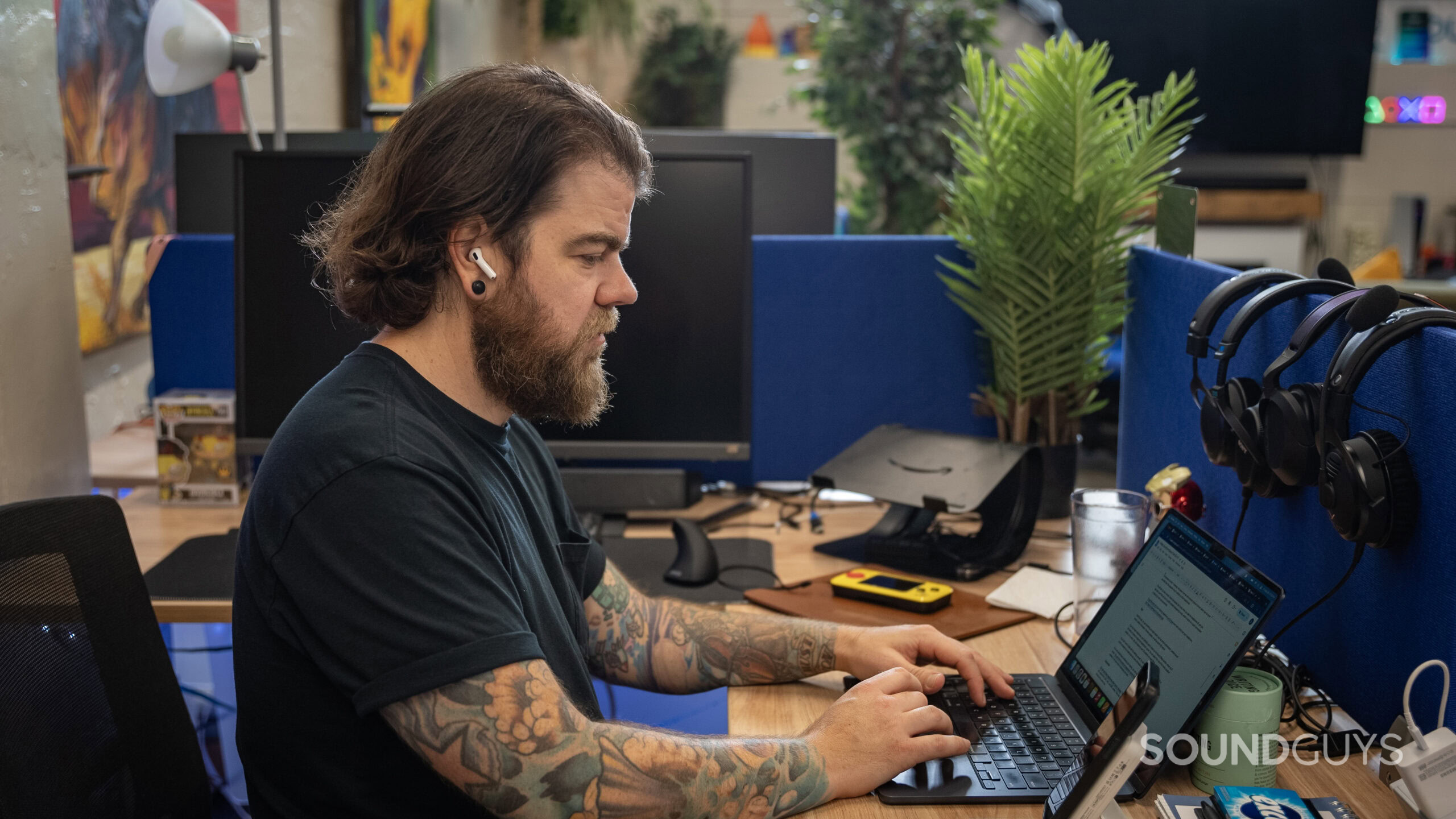 Apple AirPods 4 side profile man wearing while working at office desk A man wears an Apple AirPods 4 with Active Noise Cancellation earbud while working at a desk.