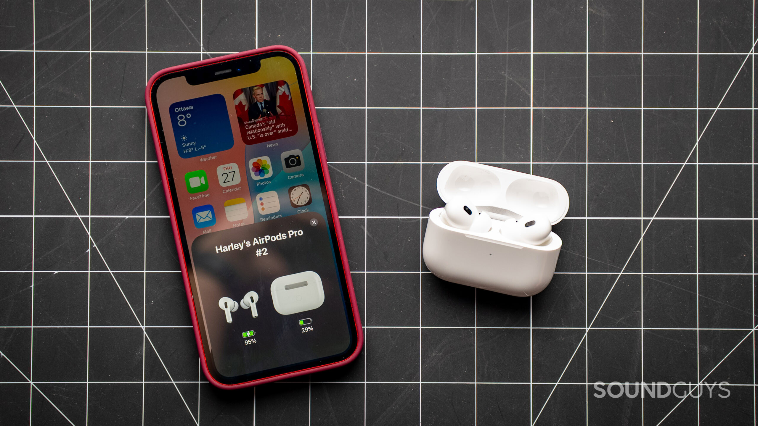 apple airpods pro 2 on table with iphone charging The Apple AirPods Pro 2 next to an iPhone showing the charging and battery status of the earbuds and charging case.