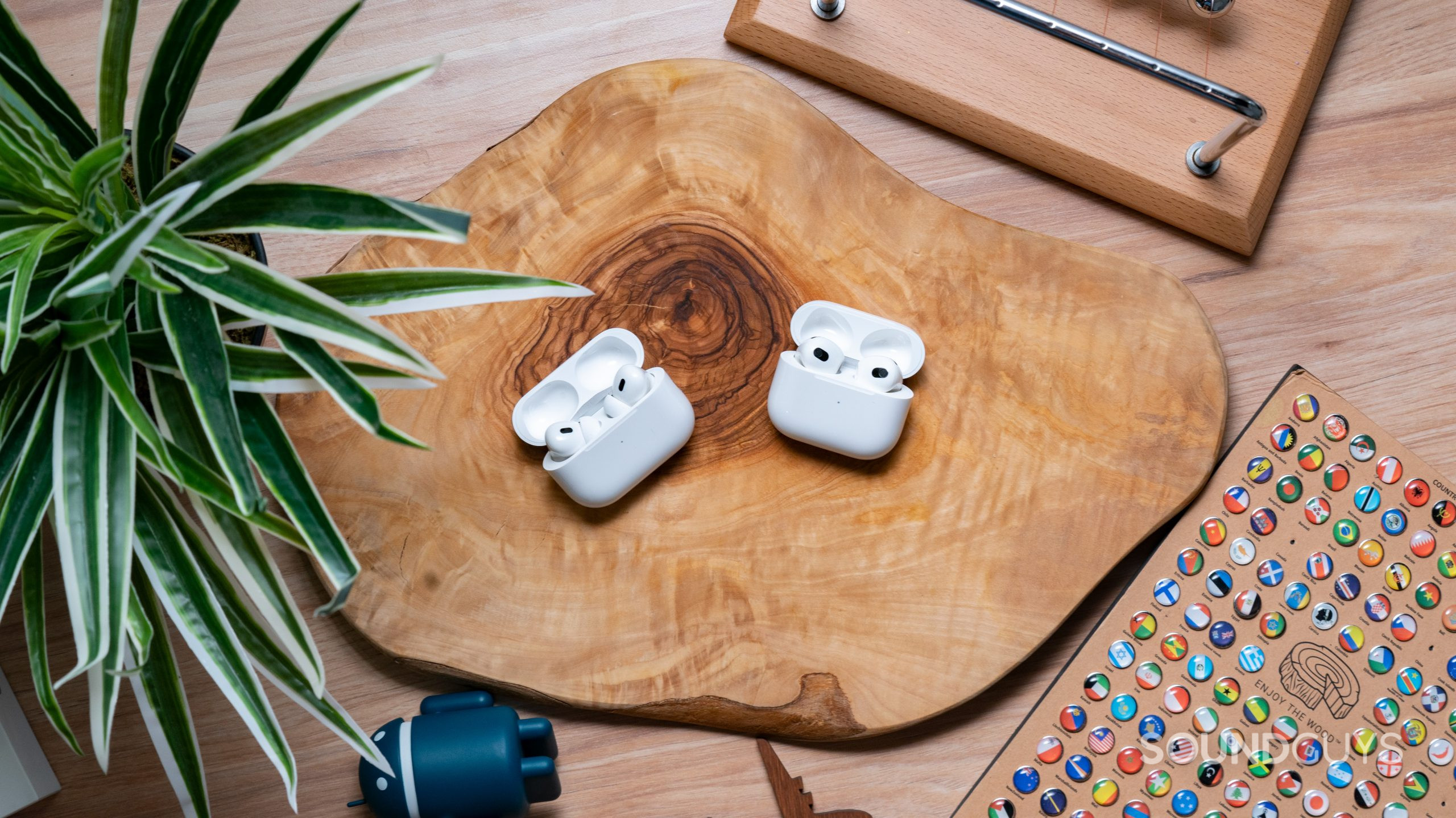 Apple Airpods Pro Gen 2 vs. Apple Airpods Gen 3 Hero Image The Apple AirPods Pro Gen 2 and the Apple AirPods Gen 3 sitting across from each other with their cases open on top of a wooden surface.