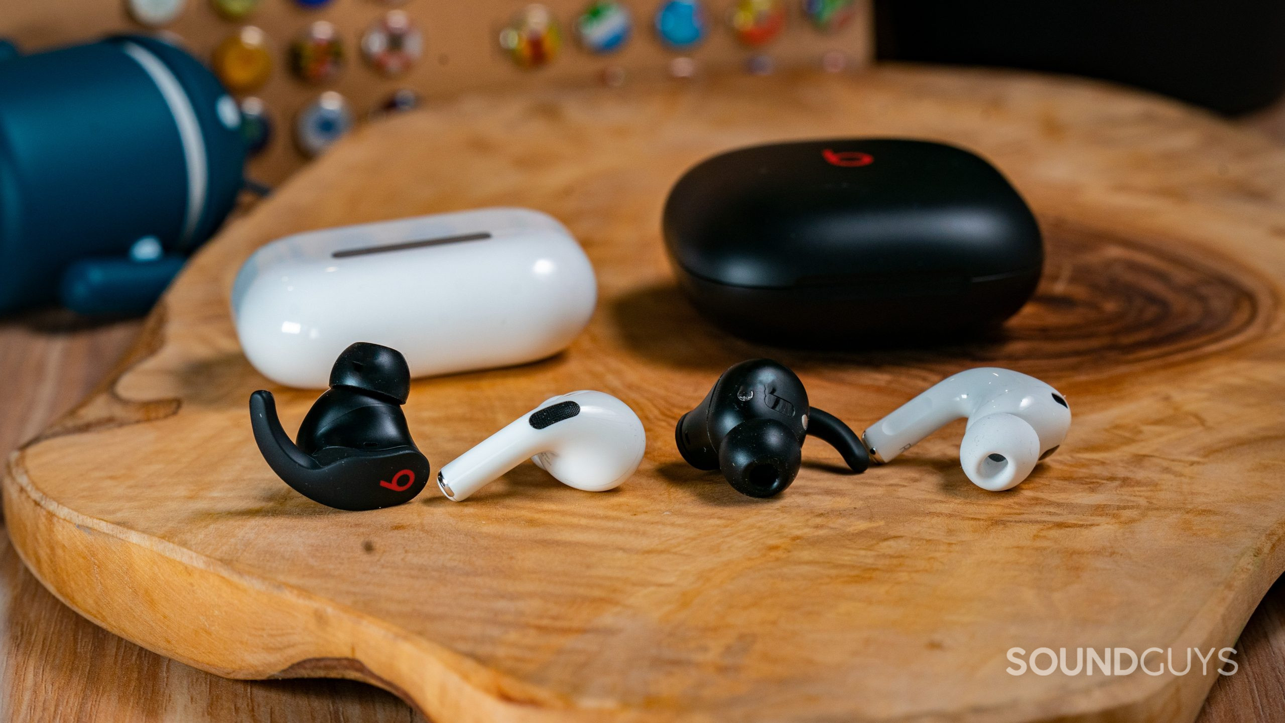 Apple Airpods Pro Gen 2 vs. Beats Fit Pro Buds Comparison The AirPods Pro (2nd generation) and Beats Fit Pro earbuds and cases next to each other on a wooden surface.