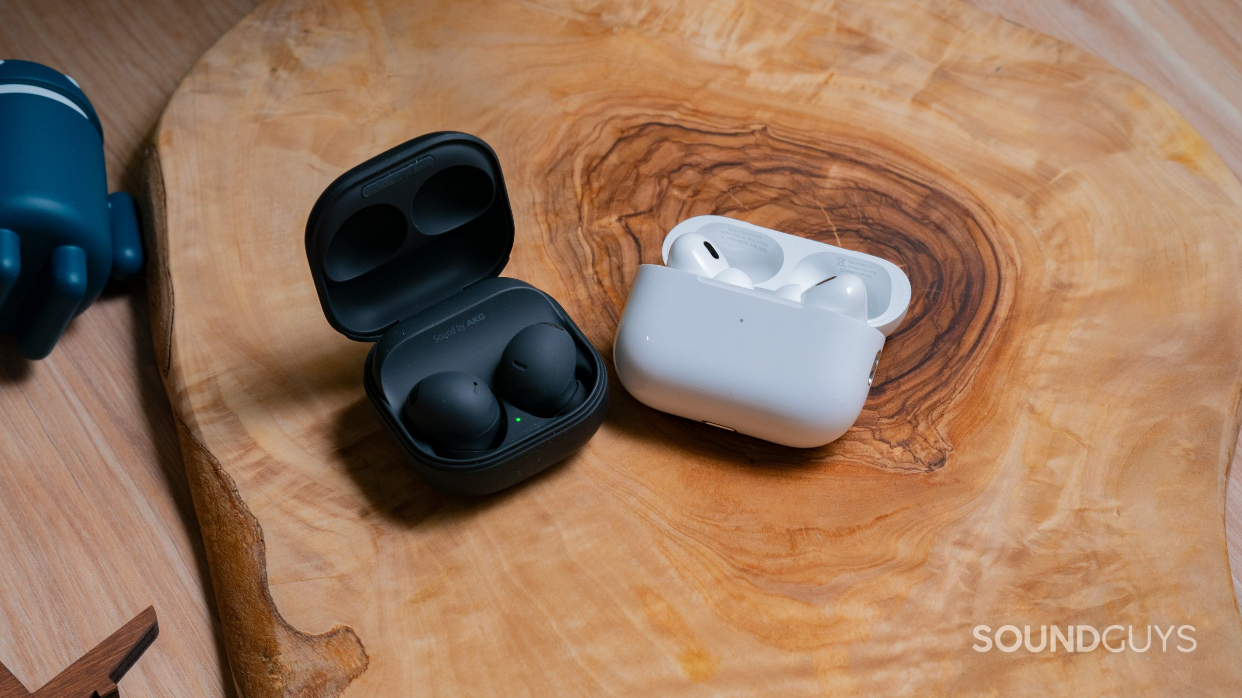 Apple Airpods Pro Gen 2 vs. Samsung Galaxy Buds 2 Pro Hero Image The open cases of the Samsung Galaxy Buds 2 Pro sit next to the Apple AirPods Pro (2nd generation) on a wood surface.