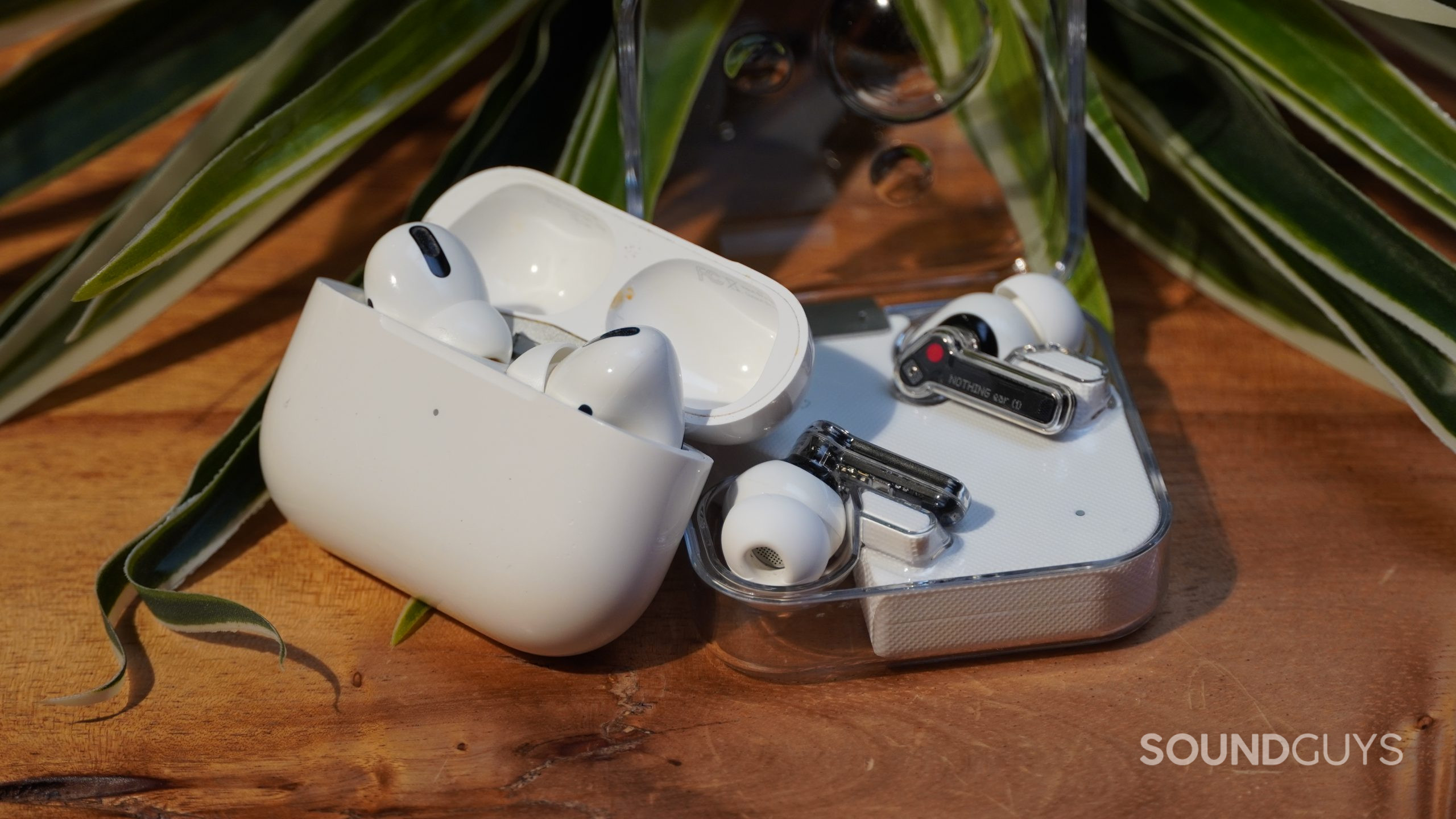 Apple AirPods Pro vs Nothing Ear 1 earbuds against eachother Apple AirPods Pro leaning against Nothing Ear 1 on a table with a plant