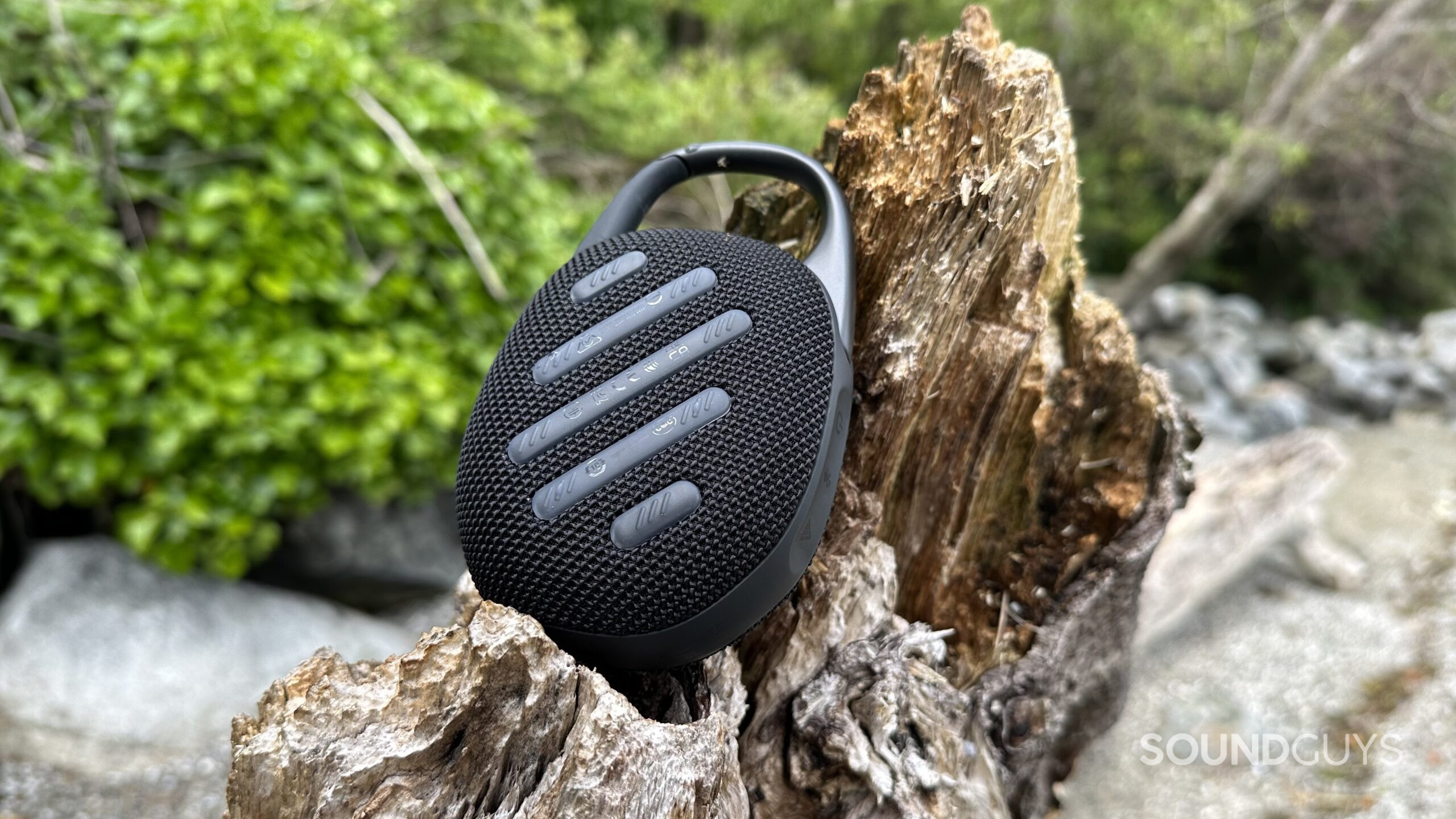 JBL Clip 5 reversed A JBL Clip 5 resting on a piece of beach driftwood, showing the silicon padding backside.
