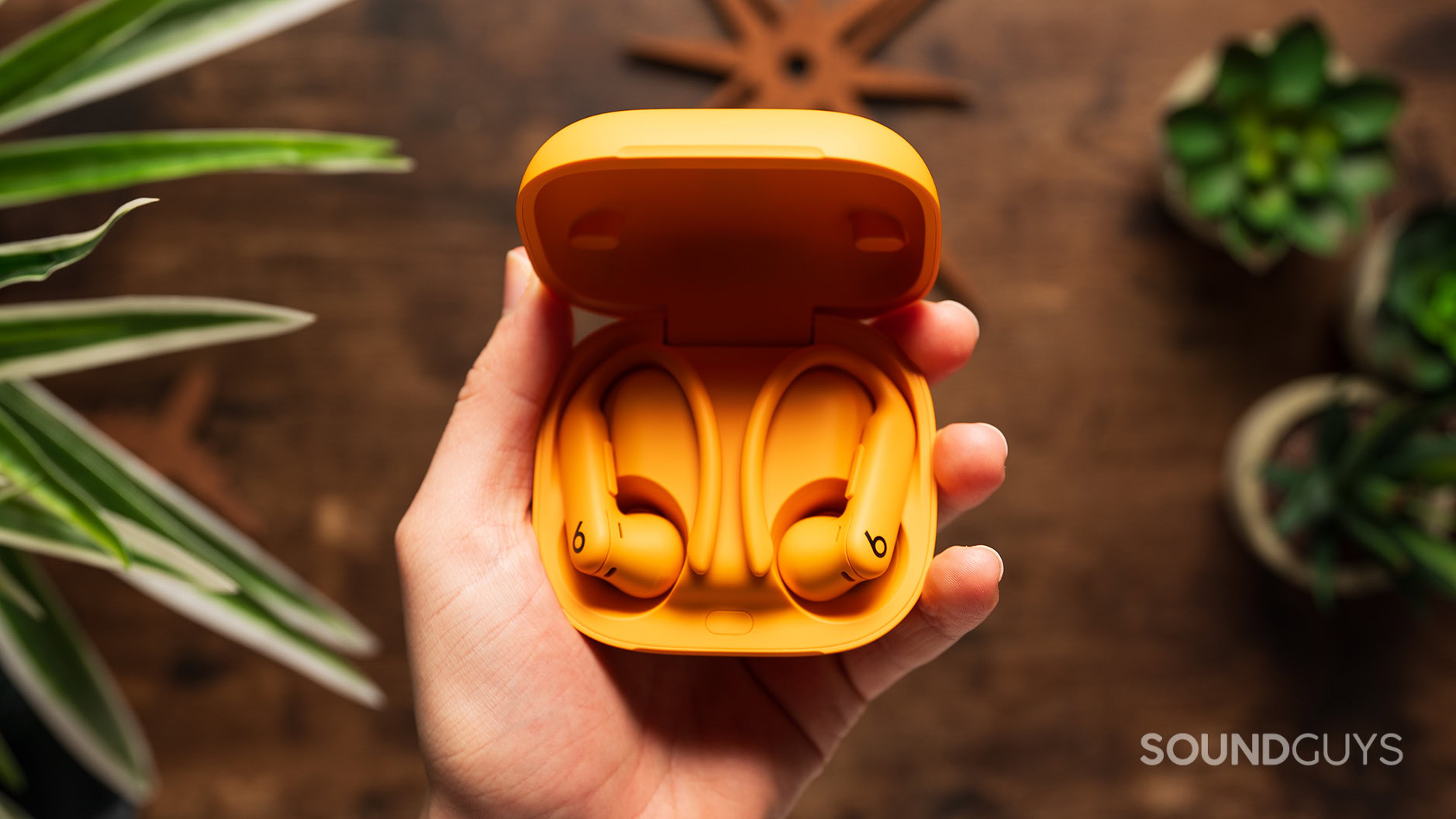 Beats Powerbeats Pro 2 in case above table A hand holds the Powerbeats Pro 2 earbuds in case.