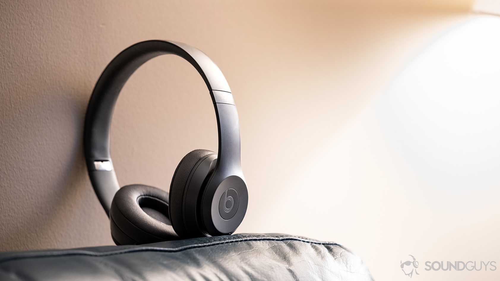 Beats Solo3 Wireless-on ear headphones grey The Beats Solo3 Wireless headphones standing on a couch against a warm-tinted wall.