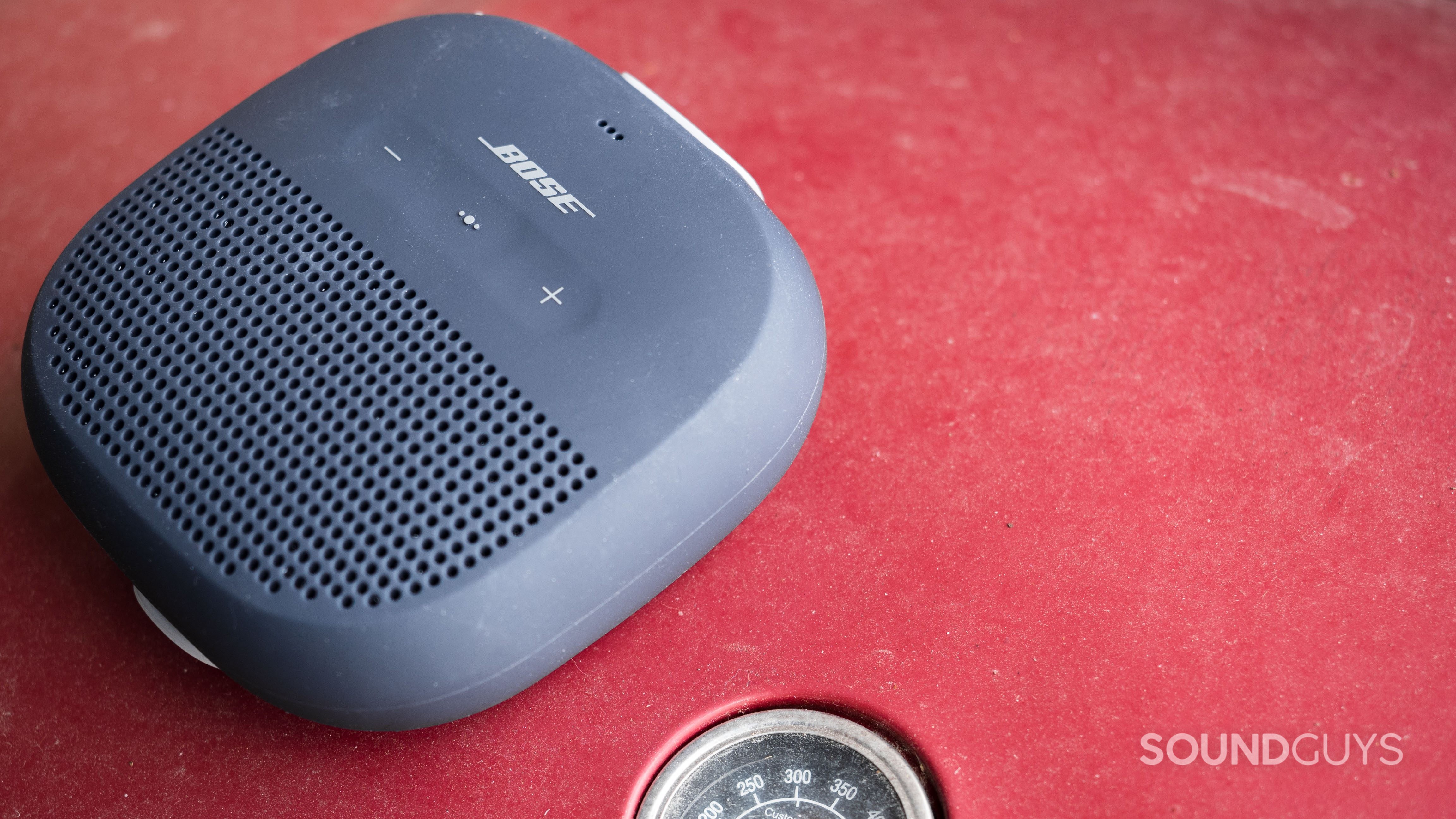 OLYMPUS DIGITAL CAMERA Bose SoundLink Micro on a red grill with the thermometer showing.