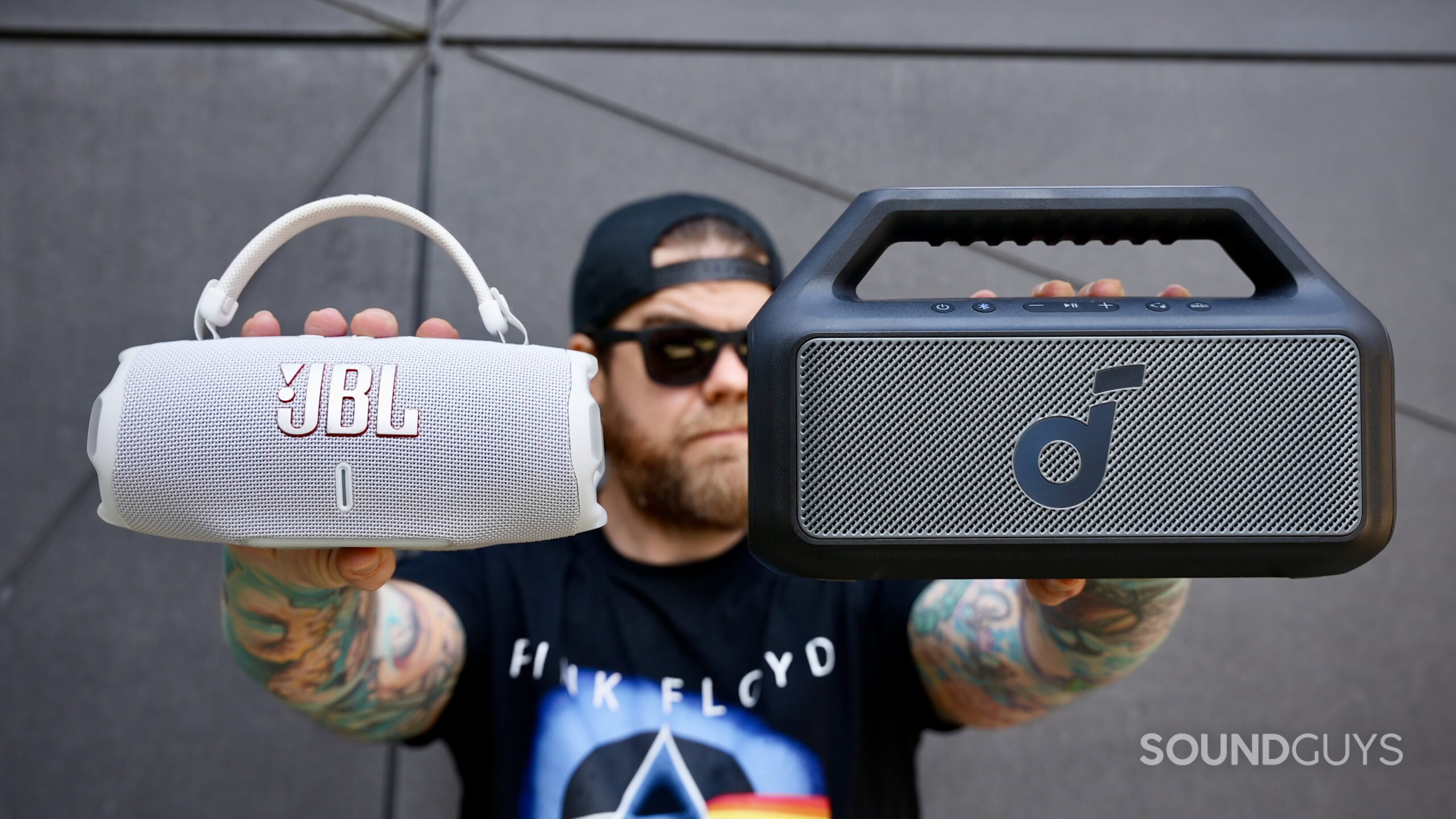 Charge 6 vs Boom 2 - 1 A man holding a JBL Charge 6 in one hand and a Soundcore Boom 2 in the other.