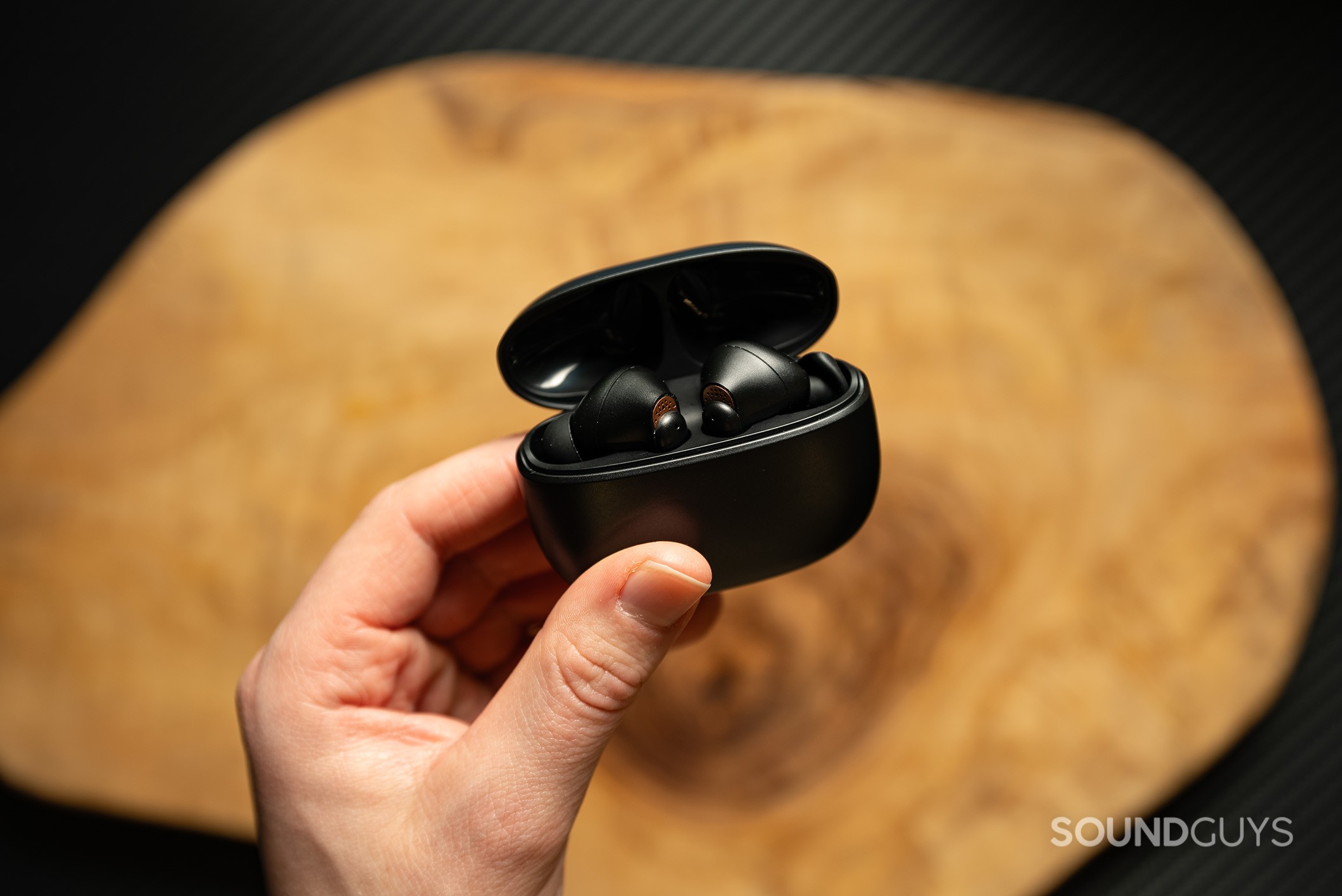 Creative Aurvana Ace Creative Aurvana Ace earbuds in charging case held by a hand above a wood table.
