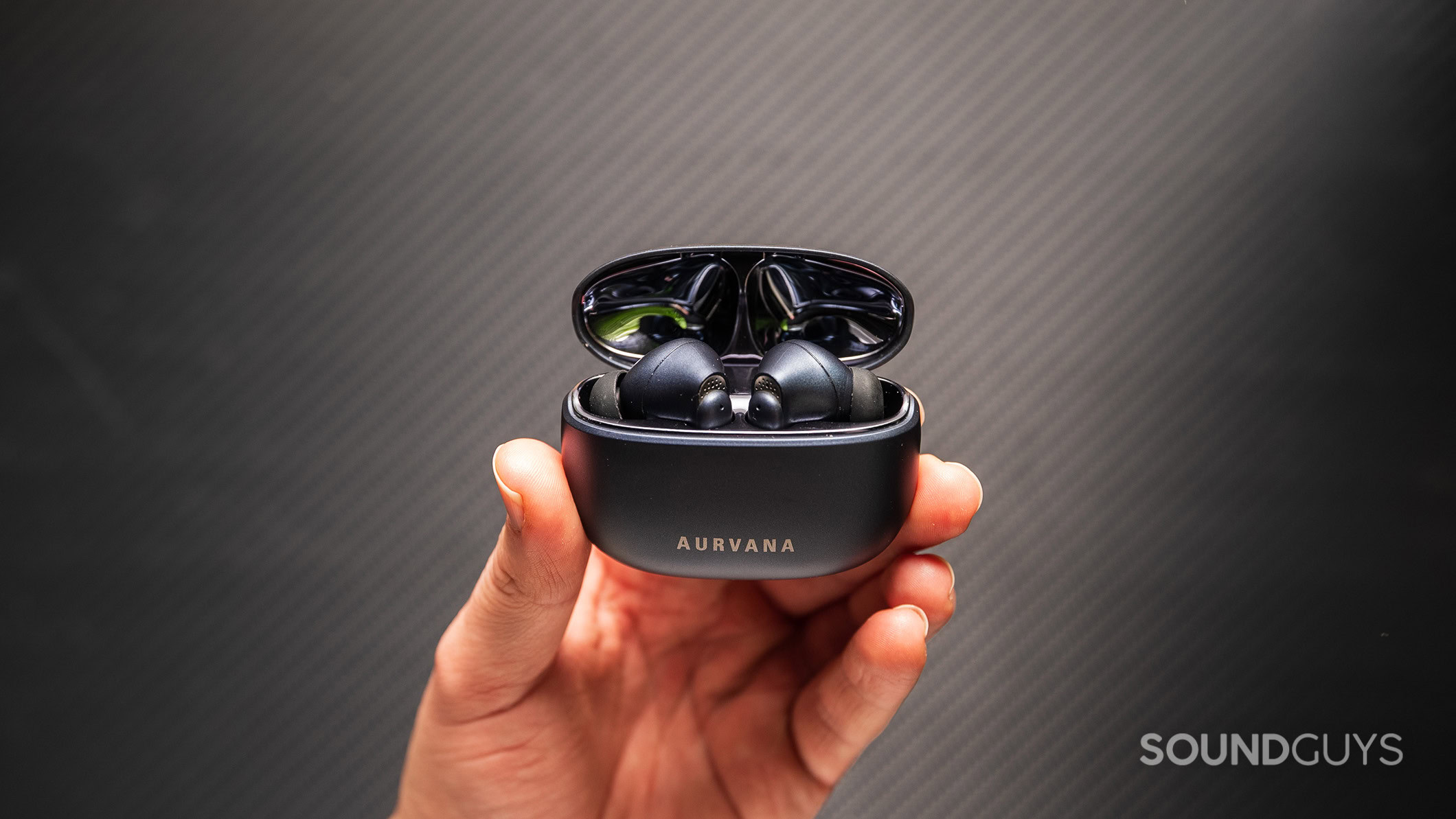 Creative Aurvana Ace Mimi earbuds in case held in hand carbon A hand holding the Creative Aurvana Ace Mimi earbuds in their charging case.