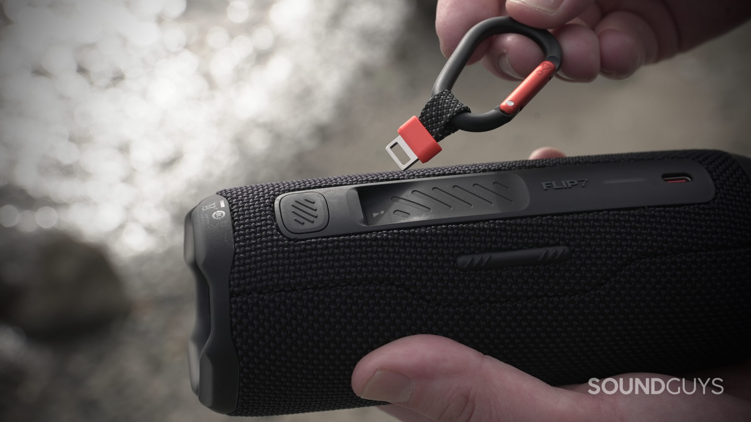 Flip 7 - 2 A pair of hands attach a carabiner clip to the JBL Flip 7 speaker.