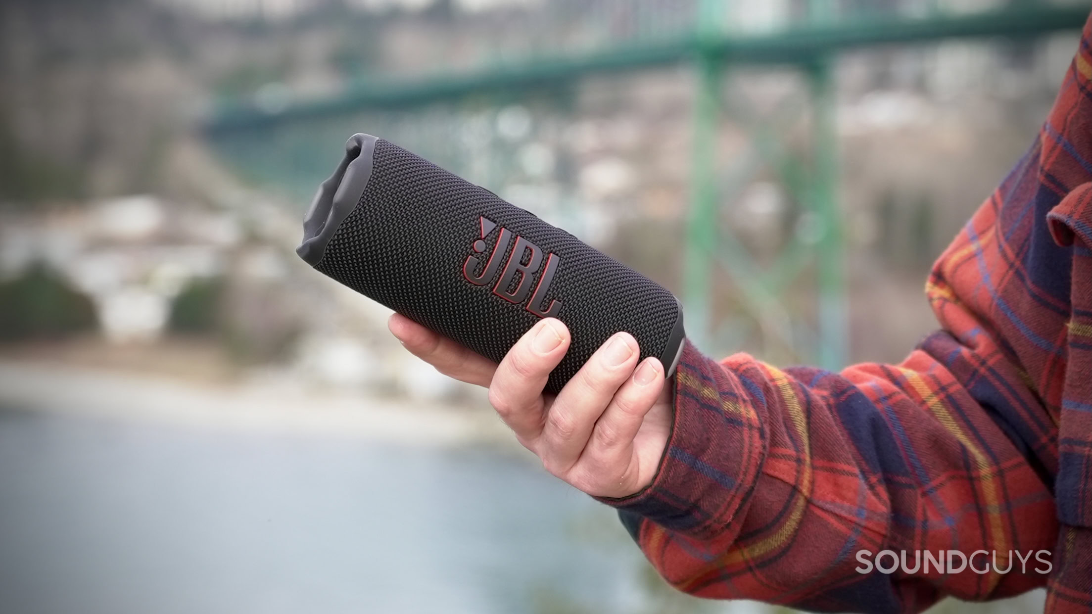 Flip 7 - 3 A man holds the JBL Flip 7 speaker with a bridge in the backround.
