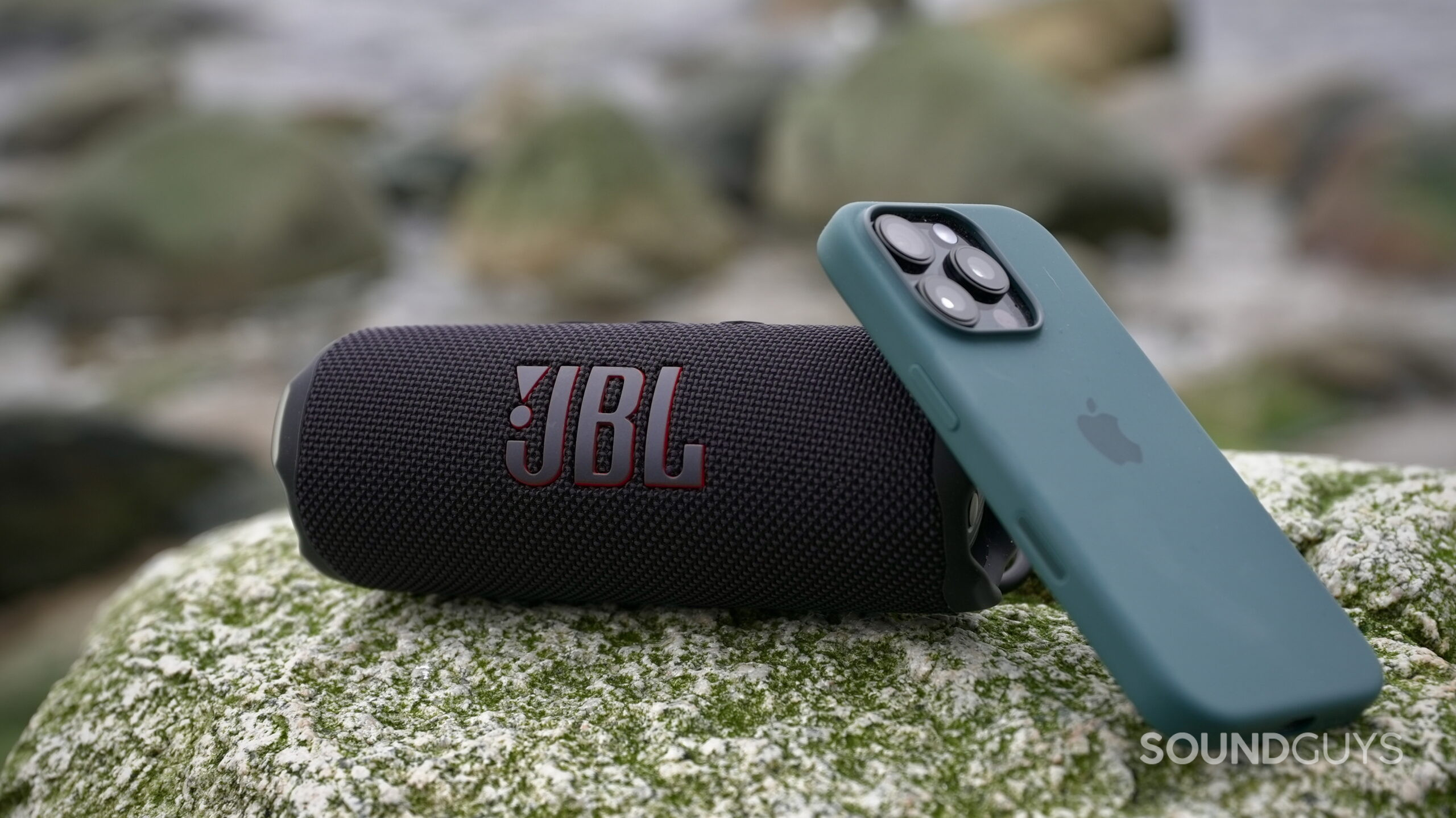 Flip 7 extra - 1 A JBL Flip 7 placed on as rock, and an iPhone 16 Pro leaving up against it.