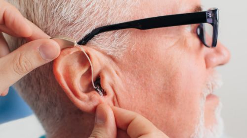 Hearing Aid Fitting Woman putting a hearing aid into a man's right ear.