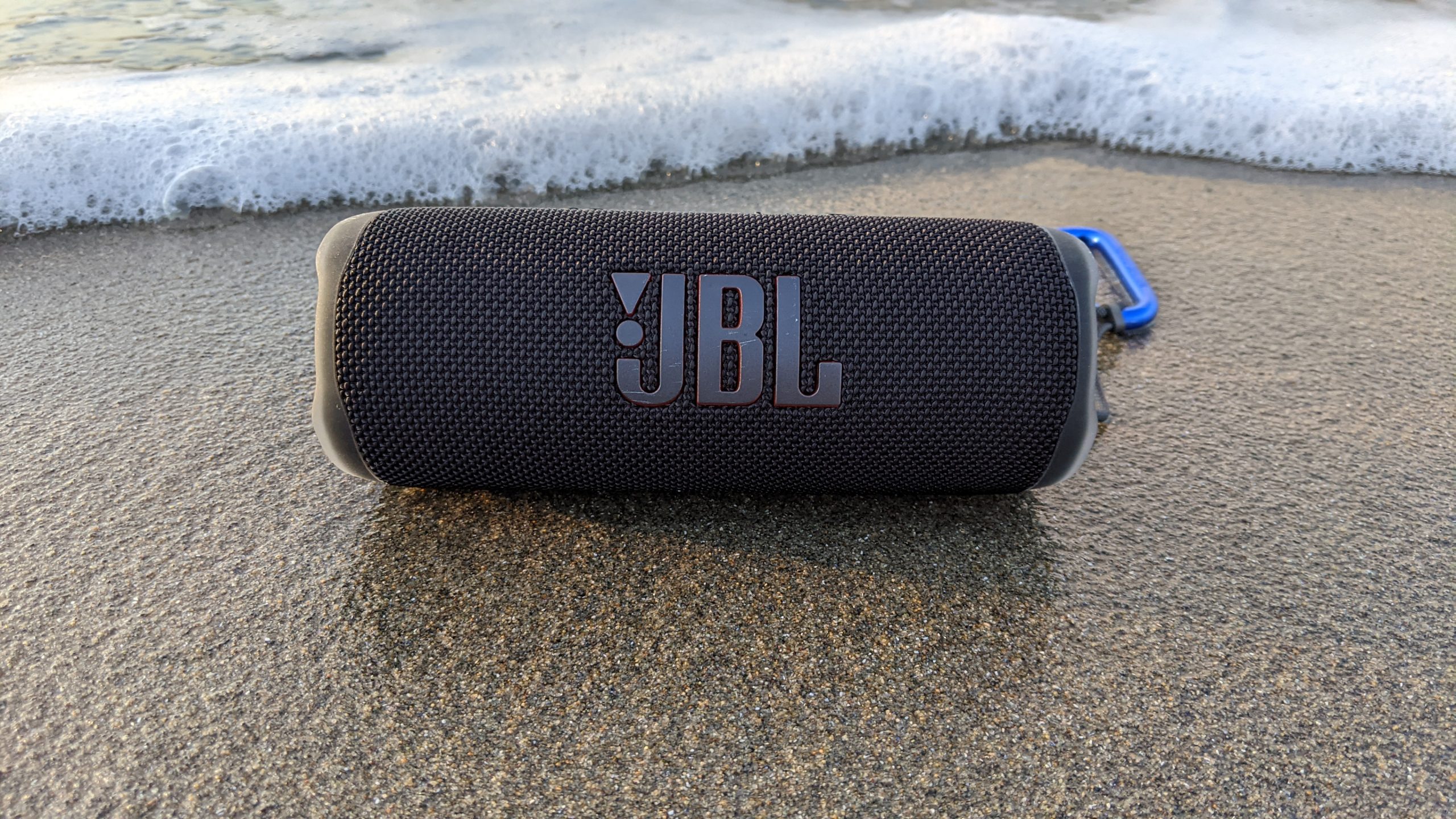 JBL Flip 6 Outdoor on Beach A JBL Flip 6 Bluetooth speaker sitting on wet sand by the ocean.