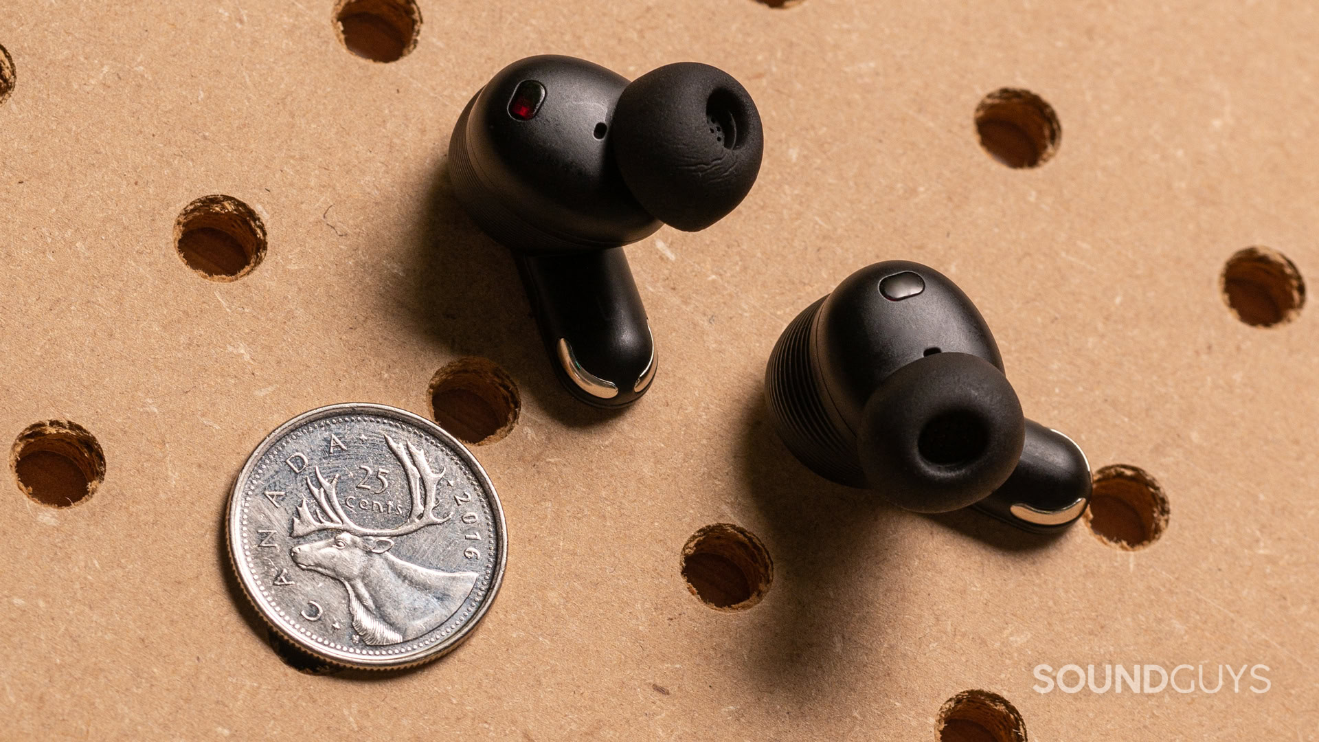 jbl-tour-pro-3-buds-alt A photo of the JBL Tour Pro 3's earbuds, next to a quarter.