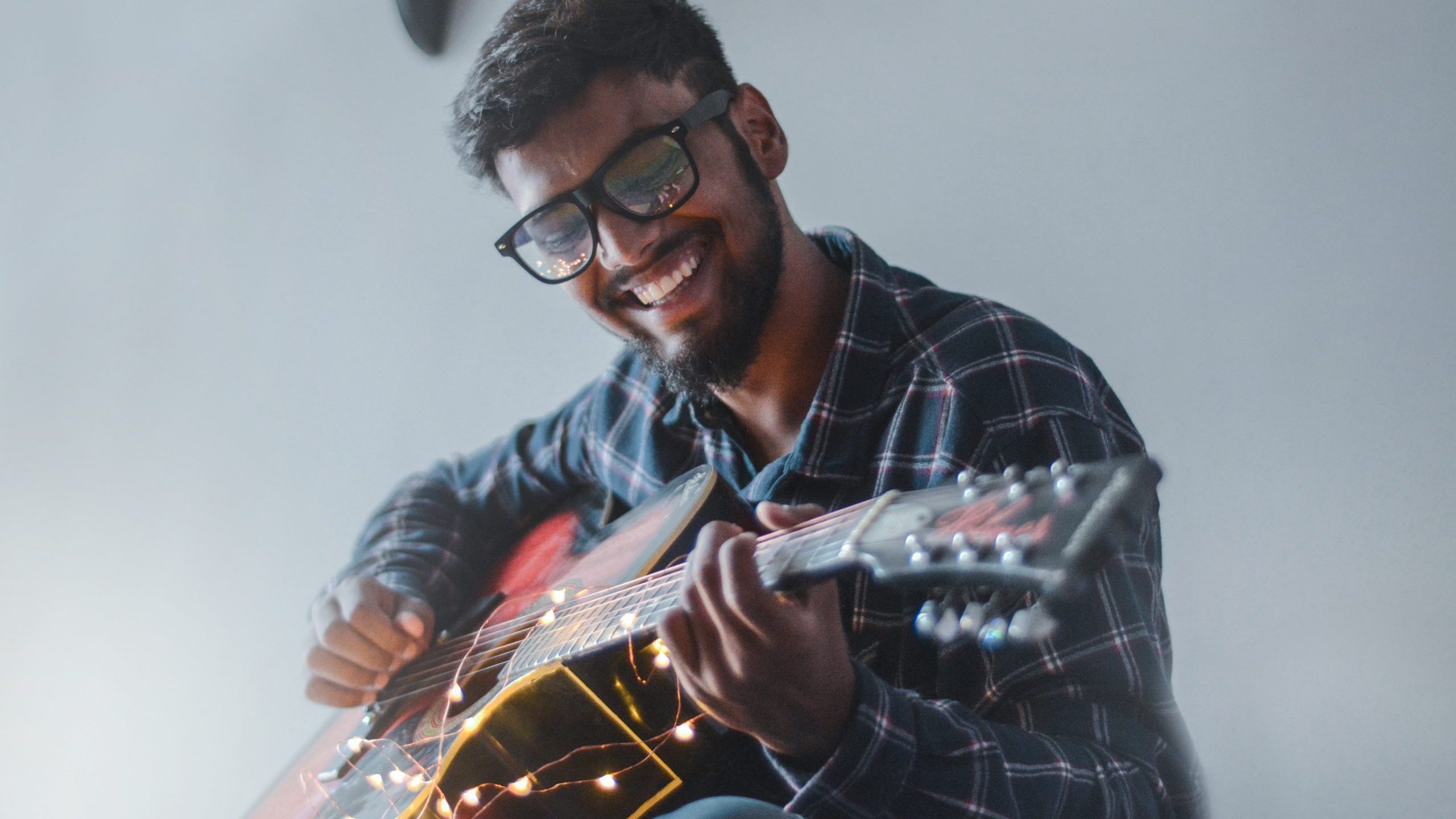 pexels-akshar-dave-977971 A man smiles while he plays guitar in an empty room.