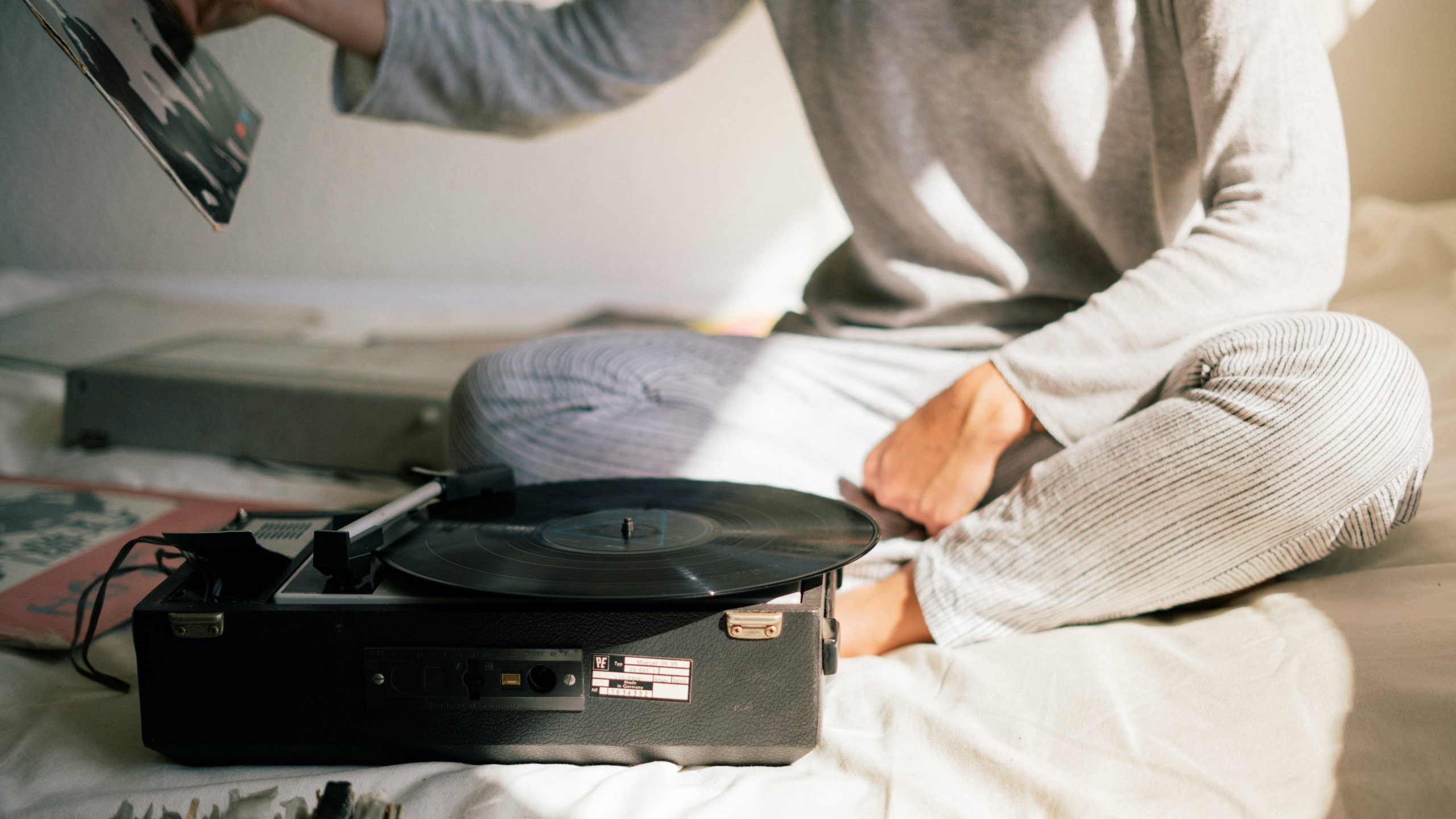 pexels-rfstudio-3618362 A person sits on a bed with vinyl records and a record-player.