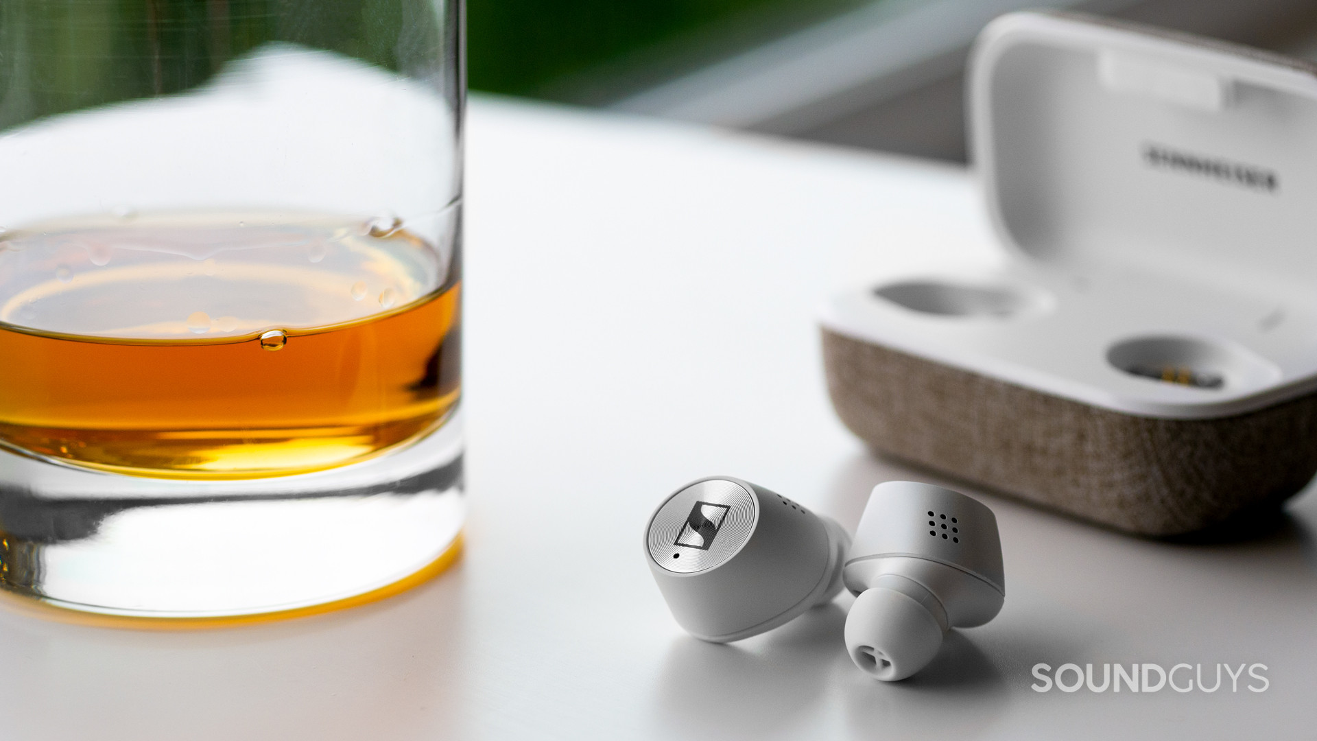 sennheiser-momentum-true-wireless-2-0-review-whiskey The Sennheiser Momentum True Wireless 2.0 on a white table next to a glass of whiskey.