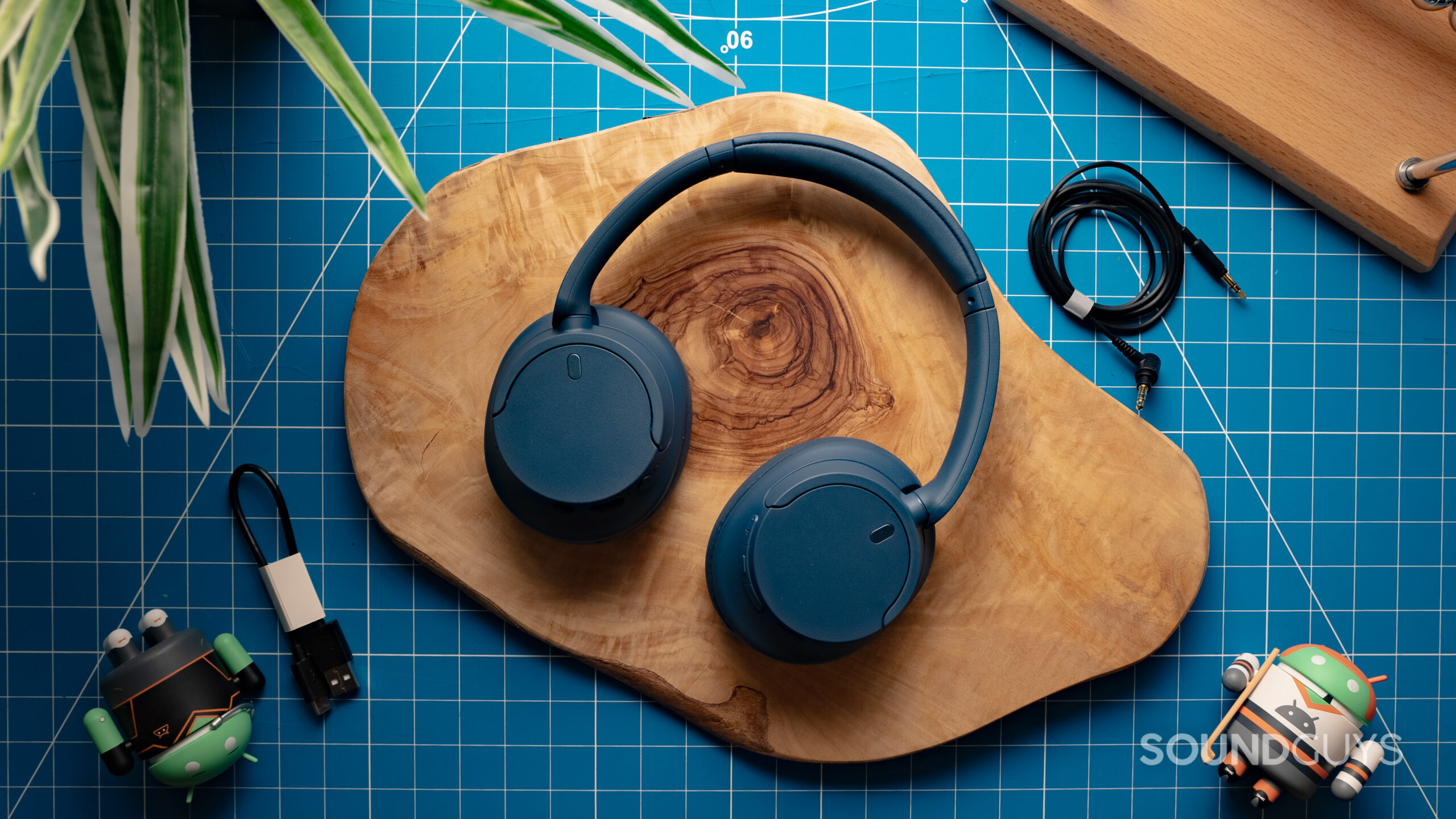 Sony-WH-CH720N-Featured-Image-#1 The Sony WH-CH720N with the ear cups rotated flat, showing the exterior plastic housing, resting on a wood surface with a grid in the background.